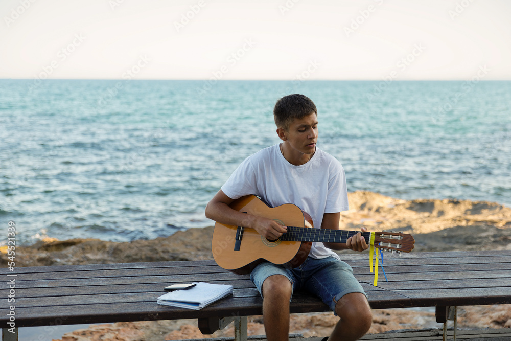 A young stylish guy plays the guitar on the embankment by the sea, the concept of music and relaxation