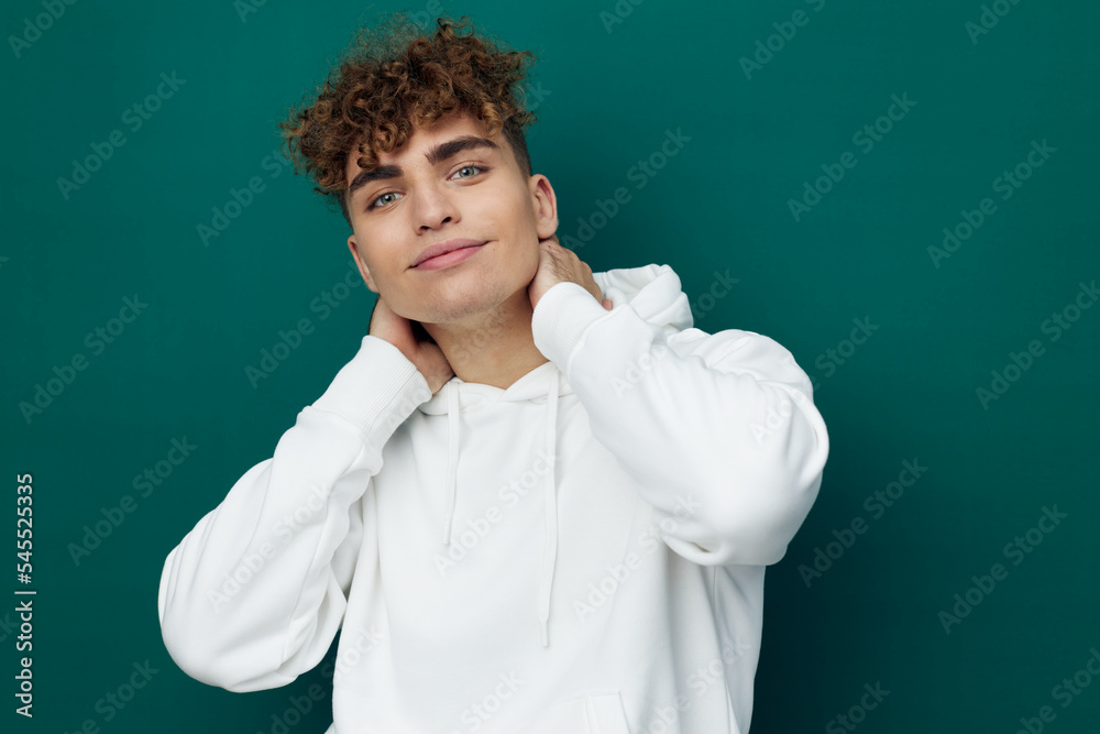 a handsome man stands on a green background in a white hoodie and poses relaxed with his hands on his neck and looking at the camera a handsome man stands on a green background in a white hoodie and poses relaxed with his hands on his neck and looking at the camera