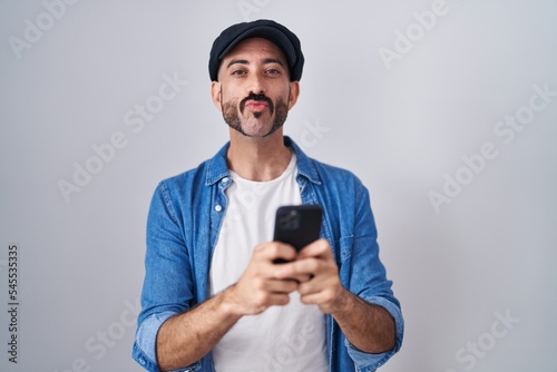 Hispanic man with beard using smartphone typing message looking at the camera blowing a kiss being lovely and sexy. love expression. © Krakenimages.com