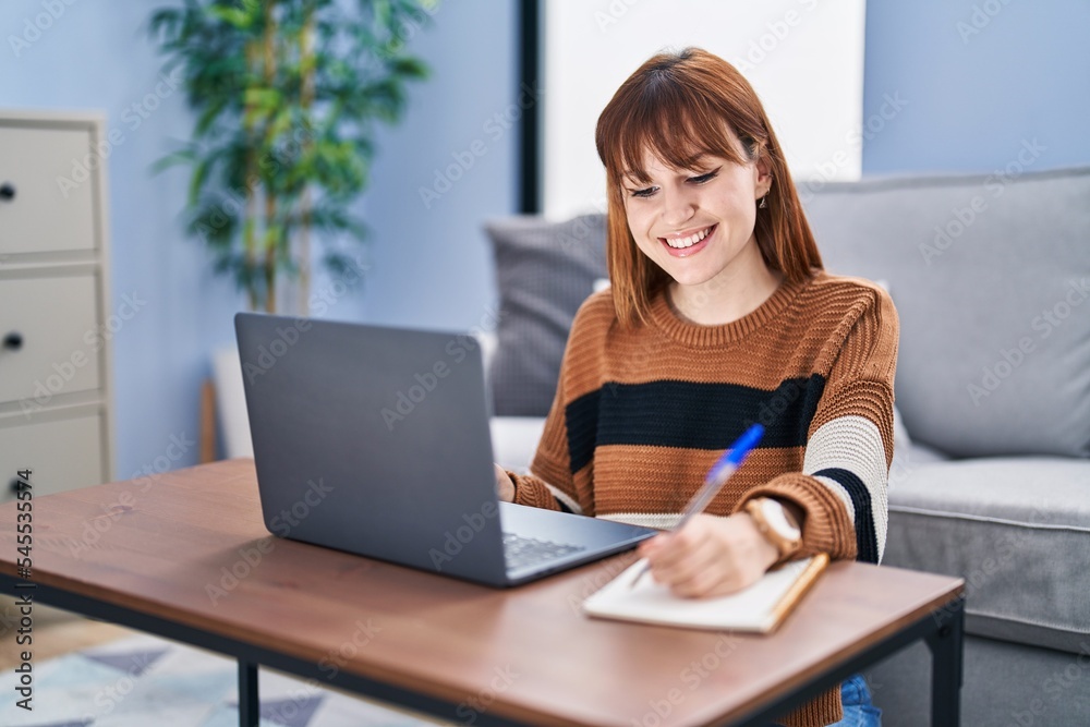 Young woman using laptop writing on notebook at home Young woman using laptop writing on notebook at home