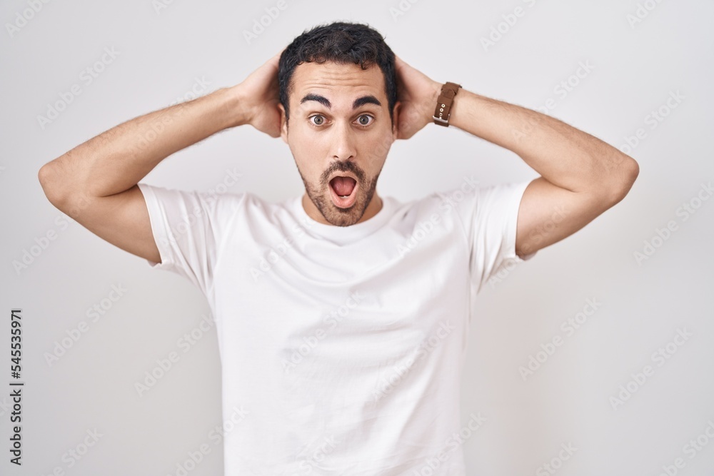 Handsome hispanic man standing over white background crazy and scared with hands on head, afraid and surprised of shock with open mouth Handsome hispanic man standing over white background crazy and scared with hands on head, afraid and surprised of shock with open mouth