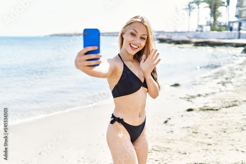 Young cuacasian girl wearing bikini having video call using smartphone at the beach.