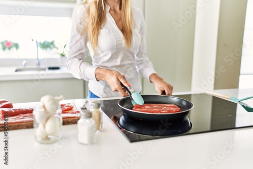 Young blonde woman cooking beef at kitchen
