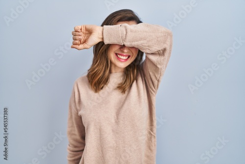 Young woman standing over isolated background covering eyes with arm smiling cheerful and funny. blind concept.
