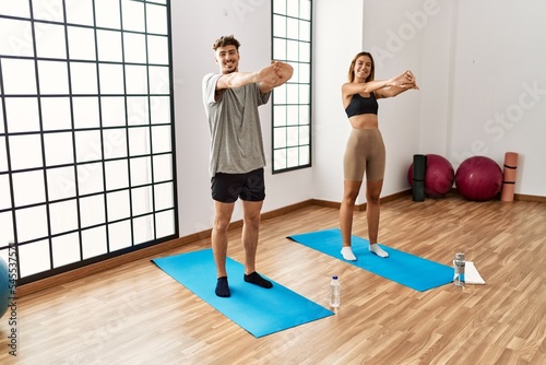 Young hispanic sporty couple smiling happy stretching at the sport center.