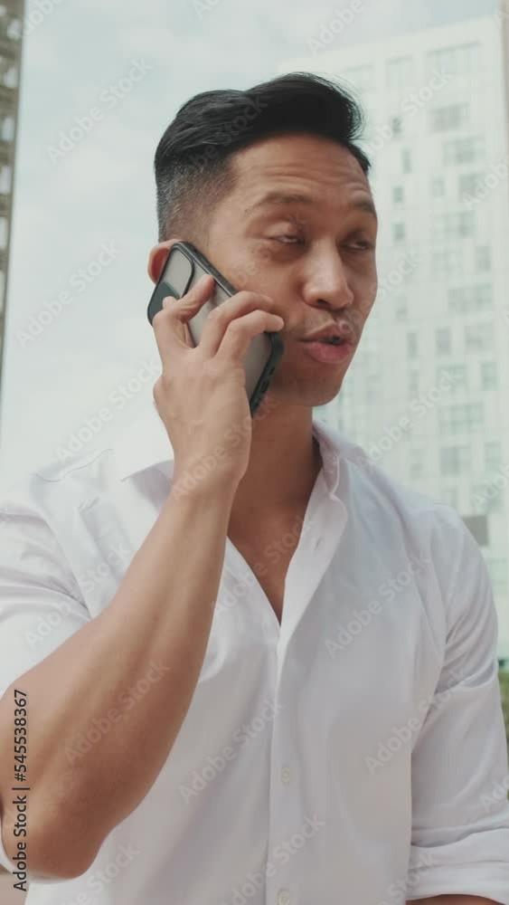 VERTICAL VIDEO: Young businessman talking on smartphone on modern buildings background VERTICAL VIDEO: Young businessman talking on smartphone on modern buildings background