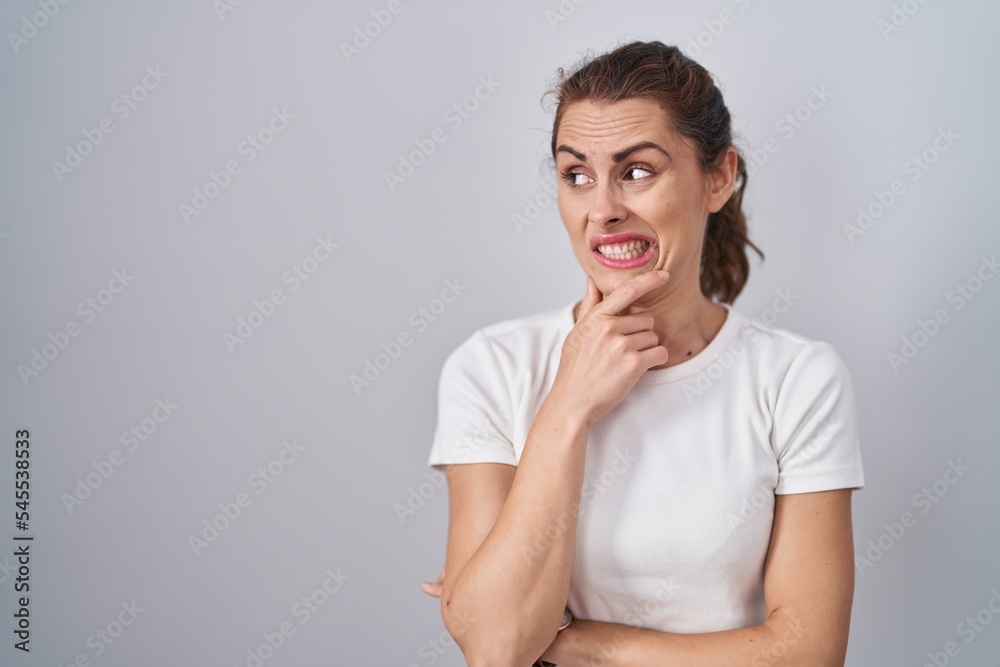 Beautiful brunette woman standing over isolated background thinking worried about a question, concerned and nervous with hand on chin Beautiful brunette woman standing over isolated background thinking worried about a question, concerned and nervous with hand on chin