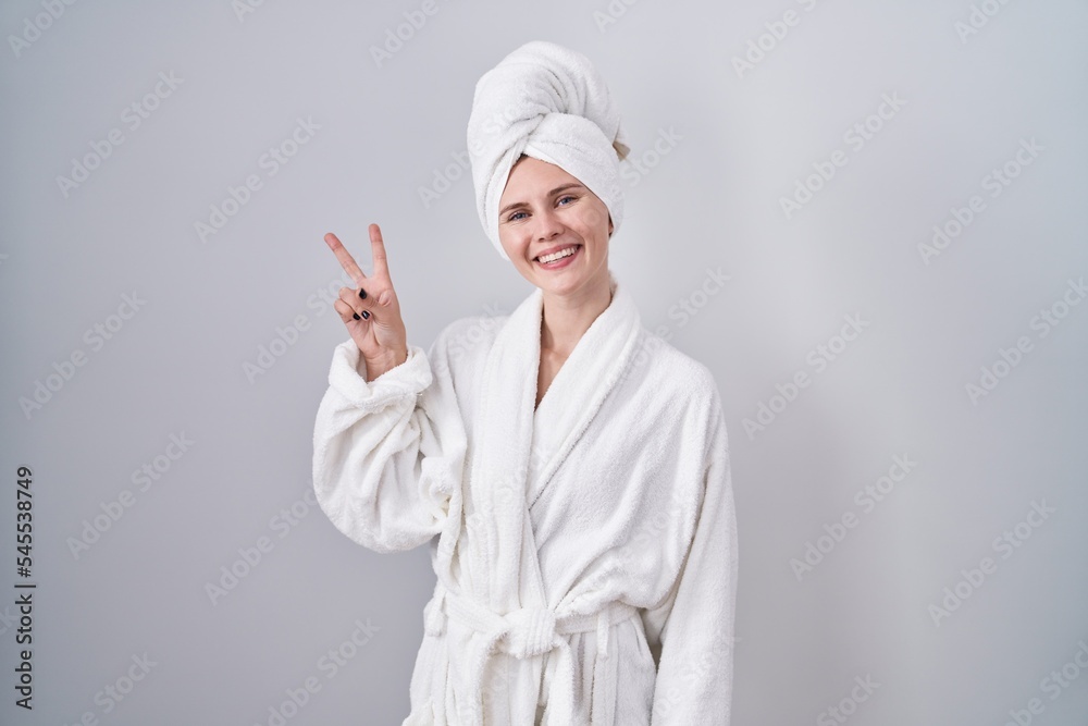 Blonde caucasian woman wearing bathrobe smiling looking to the camera showing fingers doing victory sign. number two. Blonde caucasian woman wearing bathrobe smiling looking to the camera showing fingers doing victory sign. number two.