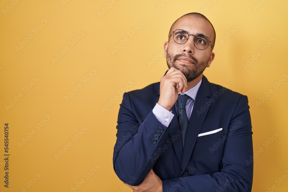 Hispanic man with beard wearing suit and tie with hand on chin thinking about question, pensive expression. smiling with thoughtful face. doubt concept.