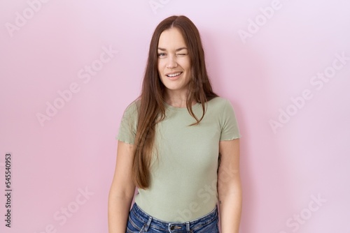 Beautiful brunette woman standing over pink background winking looking at the camera with sexy expression, cheerful and happy face.