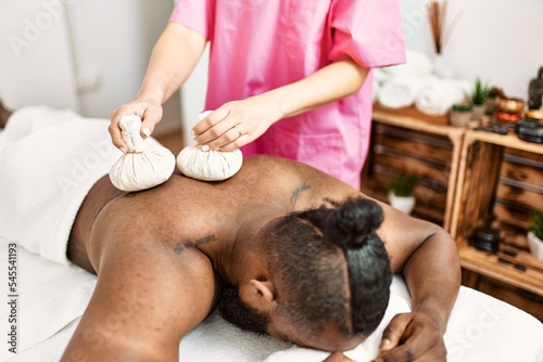 Young african american man having back massage with thai bags at beauty center