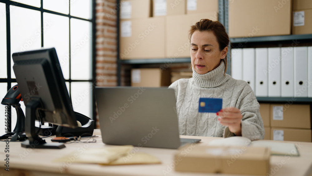 Middle age hispanic woman ecommerce business worker using laptop and credit card at storehouse office Middle age hispanic woman ecommerce business worker using laptop and credit card at storehouse office