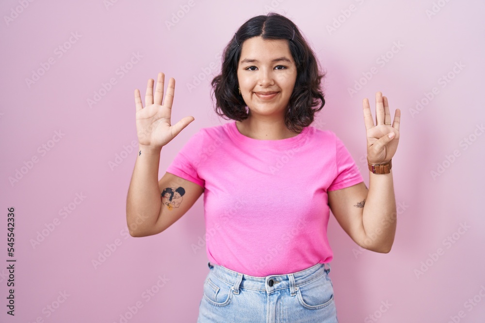 Young hispanic woman standing over pink background showing and pointing up with fingers number nine while smiling confident and happy. Young hispanic woman standing over pink background showing and pointing up with fingers number nine while smiling confident and happy.