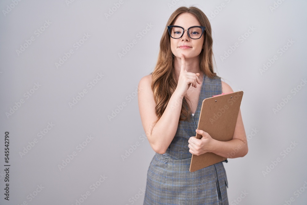 Caucasian woman wearing glasses and business clothes thinking concentrated about doubt with finger on chin and looking up wondering Caucasian woman wearing glasses and business clothes thinking concentrated about doubt with finger on chin and looking up wondering