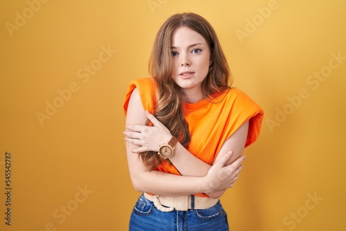 Caucasian woman standing over yellow background shaking and freezing for winter cold with sad and shock expression on face