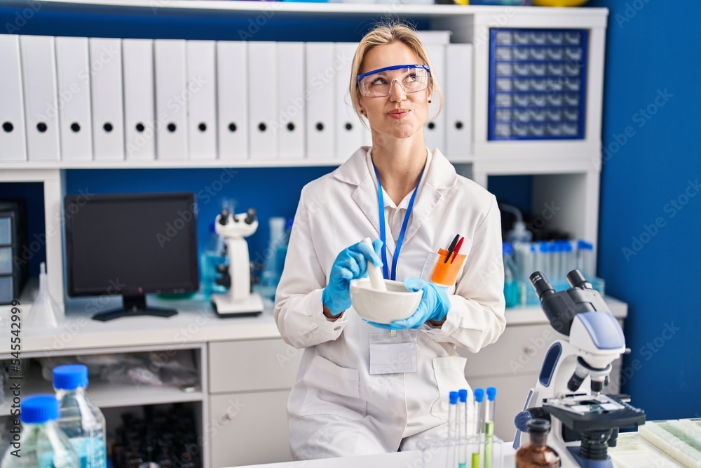 Young caucasian woman working at scientist laboratory smiling looking to the side and staring away thinking.