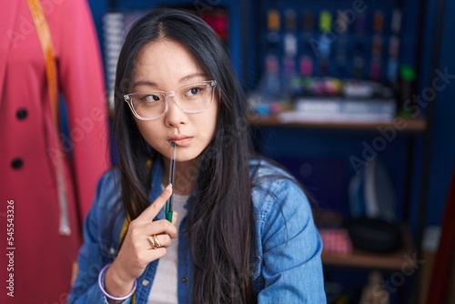 Young chinese woman tailor sitting with serious expression at clothing factory