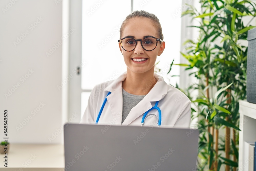 Young blonde woman wearing doctor uniform using laptop working at clinic Young blonde woman wearing doctor uniform using laptop working at clinic