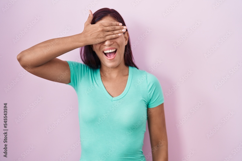 Young hispanic woman standing over pink background smiling and laughing with hand on face covering eyes for surprise. blind concept. Young hispanic woman standing over pink background smiling and laughing with hand on face covering eyes for surprise. blind concept.