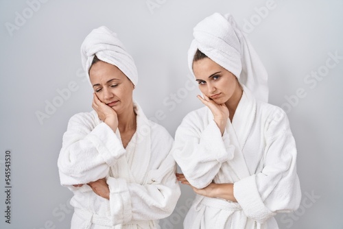 Middle age woman and daughter wearing white bathrobe and towel thinking looking tired and bored with depression problems with crossed arms.
