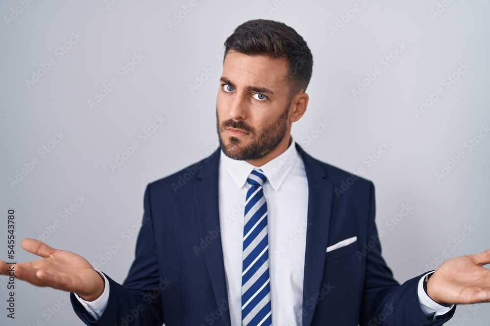 Handsome hispanic man wearing suit and tie clueless and confused with open arms, no idea concept. Handsome hispanic man wearing suit and tie clueless and confused with open arms, no idea concept.