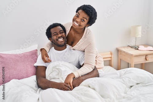 African american man and woman couple hugging each other sitting on bed at bedroom © Krakenimages.com