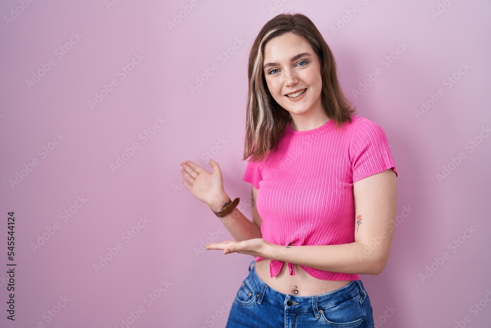 Blonde caucasian woman standing over pink background inviting to enter smiling natural with open hand Blonde caucasian woman standing over pink background inviting to enter smiling natural with open hand
