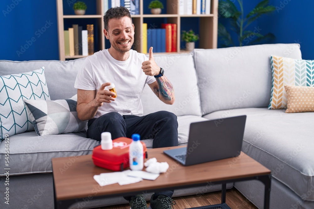 Young hispanic man watching video on laptop on how to use first aid kit smiling happy and positive, thumb up doing excellent and approval sign Young hispanic man watching video on laptop on how to use first aid kit smiling happy and positive, thumb up doing excellent and approval sign