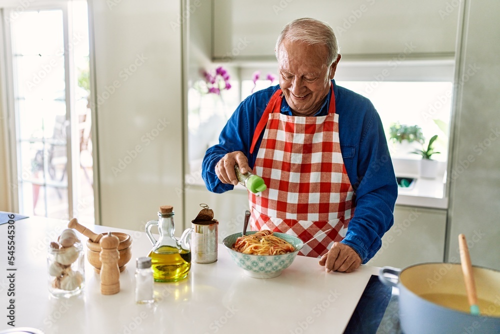 Senior man smiling confident pouring oregano on spaghetti at kitchen Senior man smiling confident pouring oregano on spaghetti at kitchen