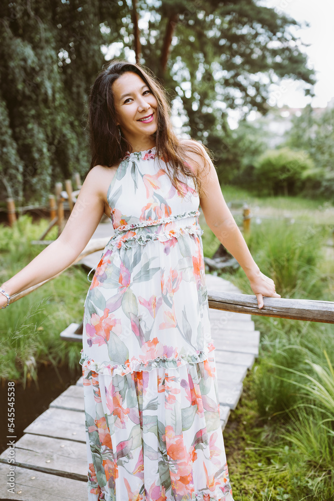 Happy multiracial Japanese woman in romantic floral maxi dress in park Happy multiracial Japanese woman in romantic floral maxi dress in park