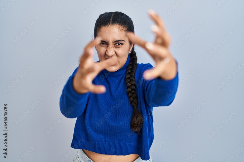 Young hispanic woman standing over isolated background shouting frustrated with rage, hands trying to strangle, yelling mad Young hispanic woman standing over isolated background shouting frustrated with rage, hands trying to strangle, yelling mad
