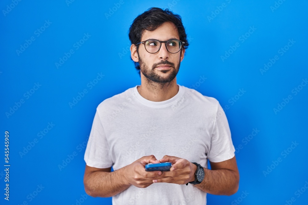 Handsome latin man using smartphone typing message smiling looking to the side and staring away thinking. Handsome latin man using smartphone typing message smiling looking to the side and staring away thinking.