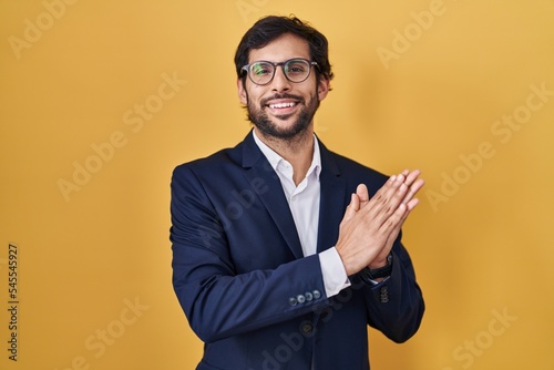 Handsome latin man standing over yellow background clapping and applauding happy and joyful, smiling proud hands together