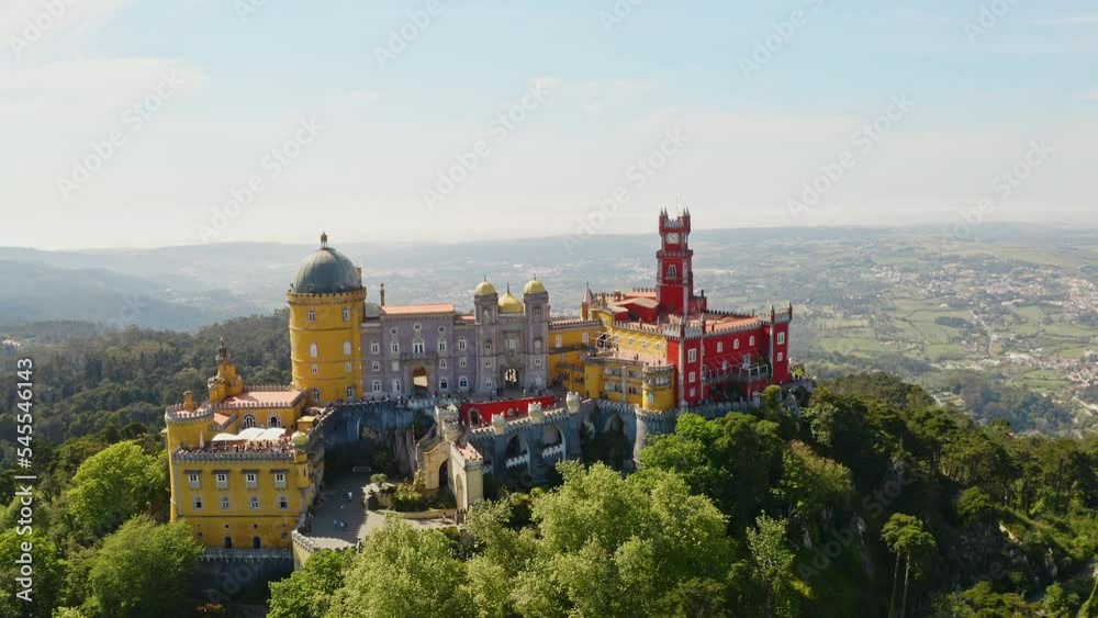 Drone footage of Pena Palace old castle beautiful mansion stand on rocky mountain top above Sintra panoramic town in Portugal famous touristic place architecture complex concept of travel in Europe