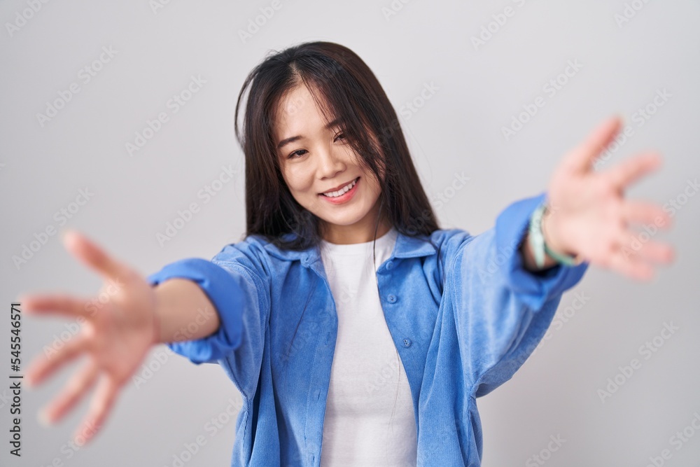Young chinese woman standing over white background looking at the camera smiling with open arms for hug. cheerful expression embracing happiness. Young chinese woman standing over white background looking at the camera smiling with open arms for hug. cheerful expression embracing happiness.