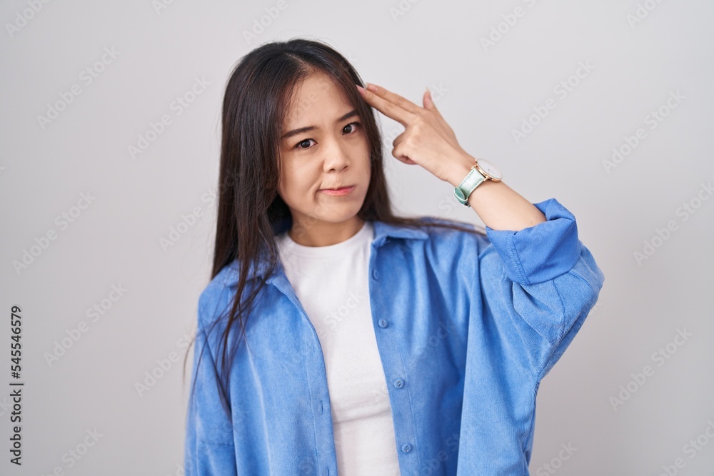 Young chinese woman standing over white background shooting and killing oneself pointing hand and fingers to head like gun, suicide gesture. Young chinese woman standing over white background shooting and killing oneself pointing hand and fingers to head like gun, suicide gesture.