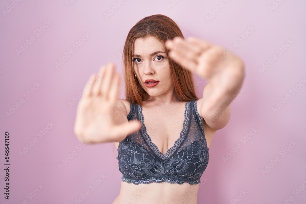 Redhead woman wearing lingerie over pink background doing frame using hands palms and fingers, camera perspective Redhead woman wearing lingerie over pink background doing frame using hands palms and fingers, camera perspective