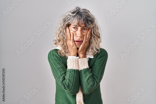 Middle age woman standing over white background tired hands covering face, depression and sadness, upset and irritated for problem