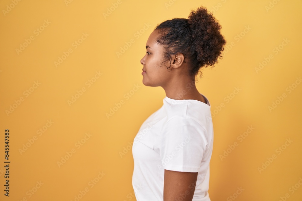 Young hispanic woman with curly hair standing over yellow background looking to side, relax profile pose with natural face and confident smile. Young hispanic woman with curly hair standing over yellow background looking to side, relax profile pose with natural face and confident smile.