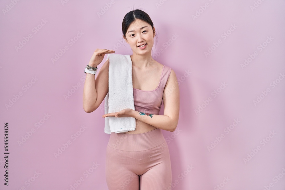 Chinese young woman wearing sportswear and towel gesturing with hands showing big and large size sign, measure symbol. smiling looking at the camera. measuring concept. Chinese young woman wearing sportswear and towel gesturing with hands showing big and large size sign, measure symbol. smiling looking at the camera. measuring concept.