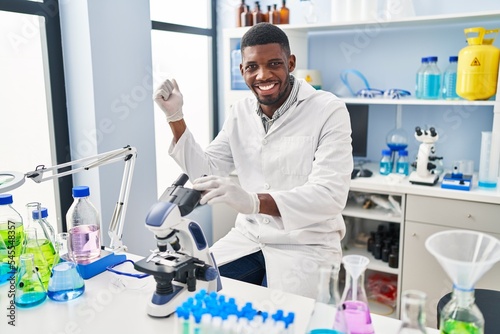 African american man working at scientist laboratory screaming proud, celebrating victory and success very excited with raised arm