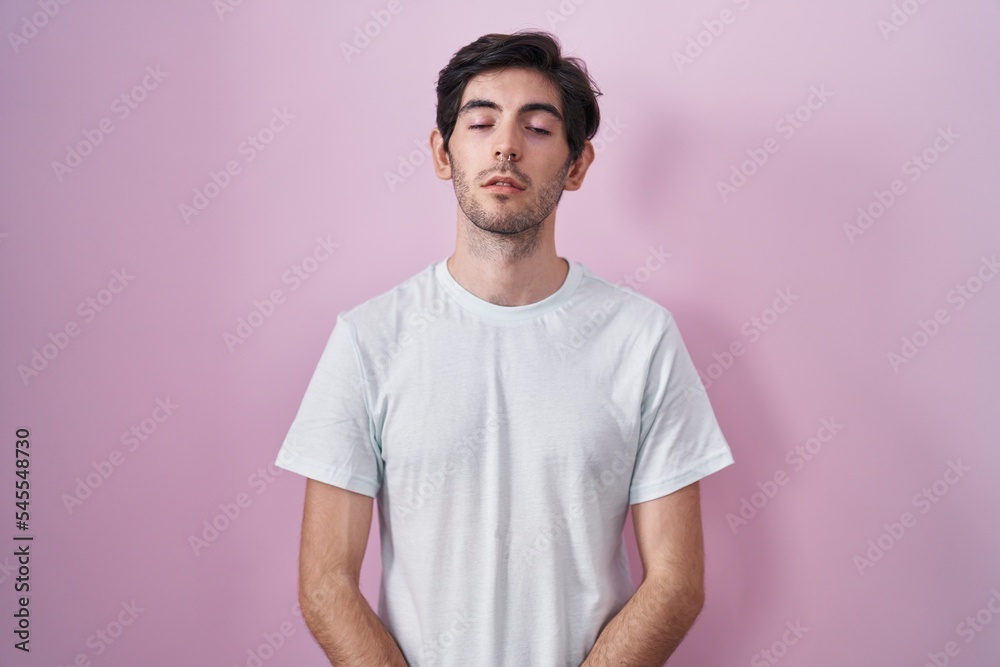 Young hispanic man standing over pink background looking sleepy and tired, exhausted for fatigue and hangover, lazy eyes in the morning.