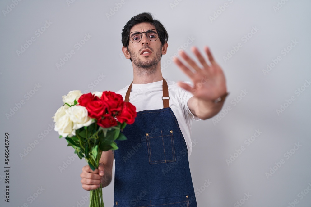 Young hispanic man holding bouquet of white and red roses doing stop gesture with hands palms, angry and frustration expression Young hispanic man holding bouquet of white and red roses doing stop gesture with hands palms, angry and frustration expression