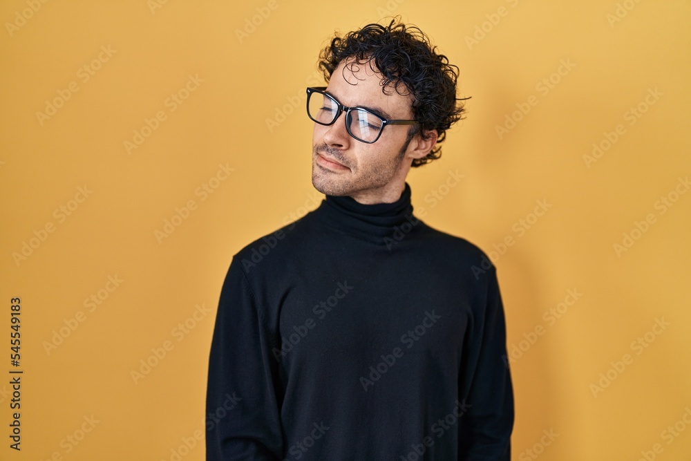 Hispanic man standing over yellow background smiling looking to the side and staring away thinking. Hispanic man standing over yellow background smiling looking to the side and staring away thinking.