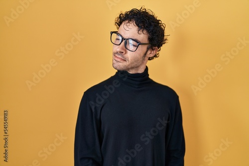 Hispanic man standing over yellow background smiling looking to the side and staring away thinking.