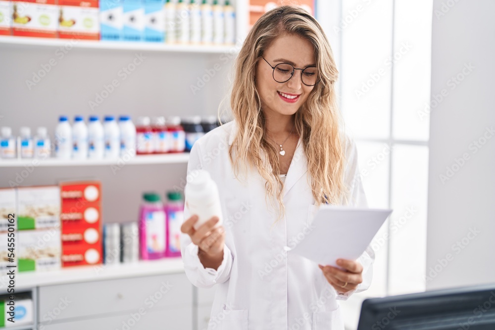Young woman pharmacist reading prescription holding pills bottle at pharmacy