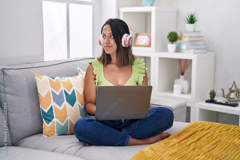 Hispanic young woman using laptop at home looking to side, relax profile pose with natural face with confident smile. Hispanic young woman using laptop at home looking to side, relax profile pose with natural face with confident smile.