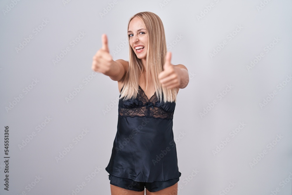 Young caucasian woman wearing nightgown approving doing positive gesture with hand, thumbs up smiling and happy for success. winner gesture. Young caucasian woman wearing nightgown approving doing positive gesture with hand, thumbs up smiling and happy for success. winner gesture.