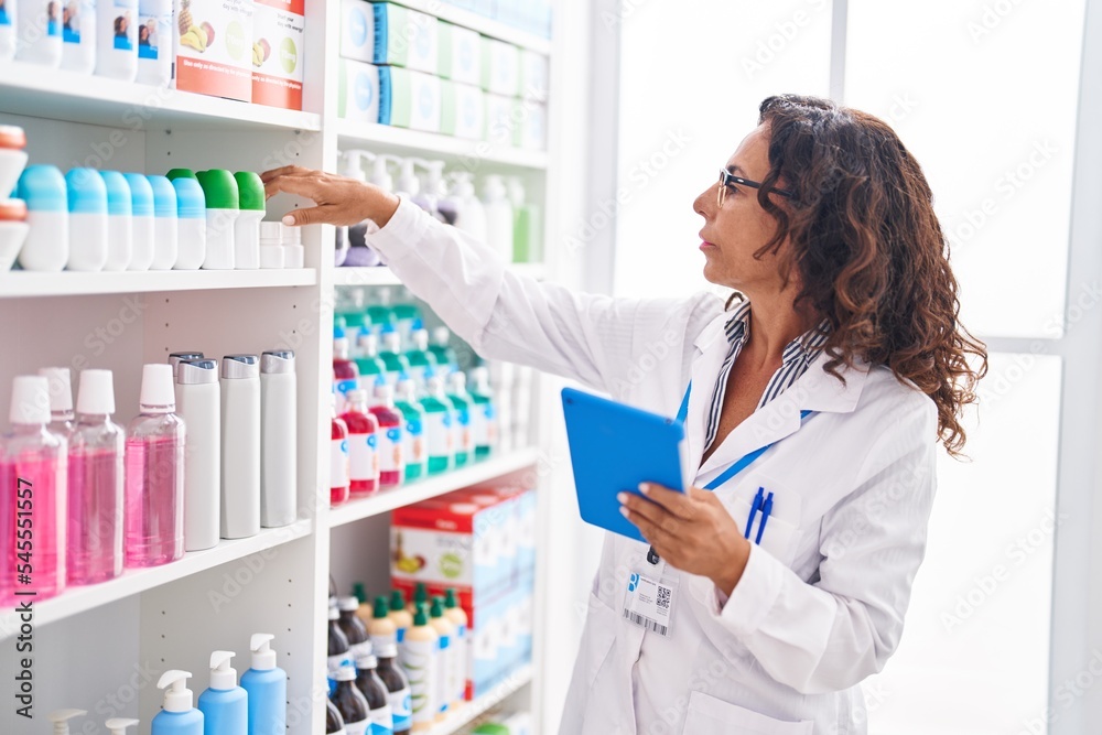 Middle age woman pharmacist using touchpad holding medicine at pharmacy