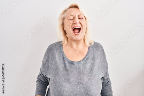 Middle age caucasian woman standing over white background angry and mad screaming frustrated and furious, shouting with anger. rage and aggressive concept.